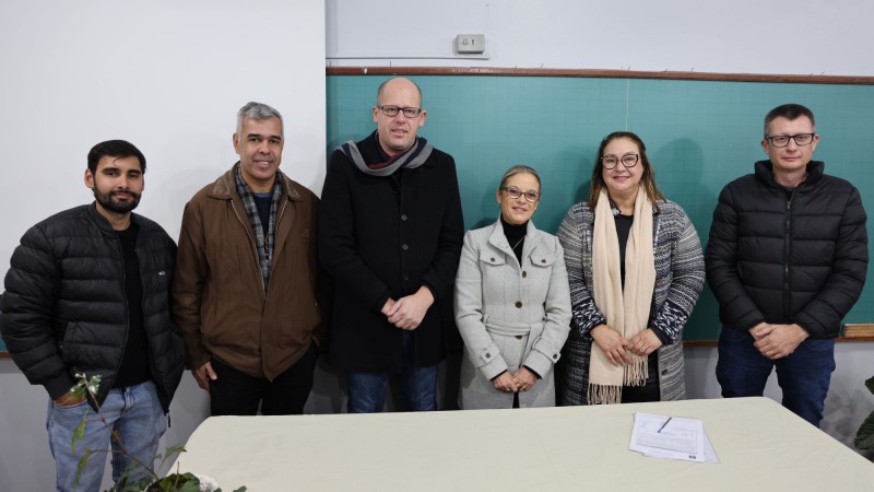 Grupo de pessoas posa para foto entre uma mesa e um quadro negro.