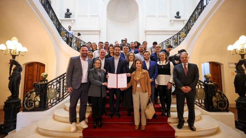 Em uma escadaria, pessoas posam para a foto. &Agrave; frente, um homem e duas mulheres ao seu lado seguram uma pasta com o contrato assinado.