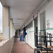 Em um corredor no segundo andar, homens de capacete trabalham pintando as paredes.