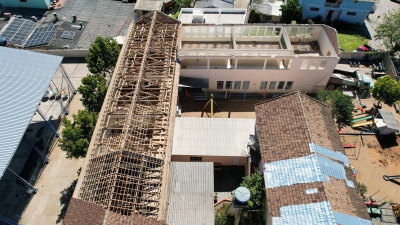 Foto a&eacute;rea dos pr&eacute;dios da escola. Dois deles, dispostos em L, est&atilde;o com o telhado total ou parcialmente retirado.