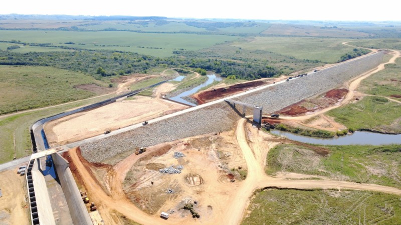 Foto a&eacute;rea da Barragem Jaguari, uma estrutura alta e comprida em meio ao campo com um arroio passando por baixo.